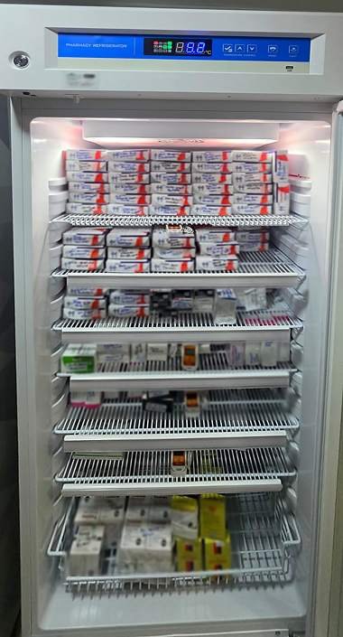 Nevera de farmacia abierta, cargada con medicamentos y con registradores de temperatura en varias repisas